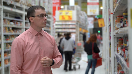 young guy chooses jam in a store or supermarket.
