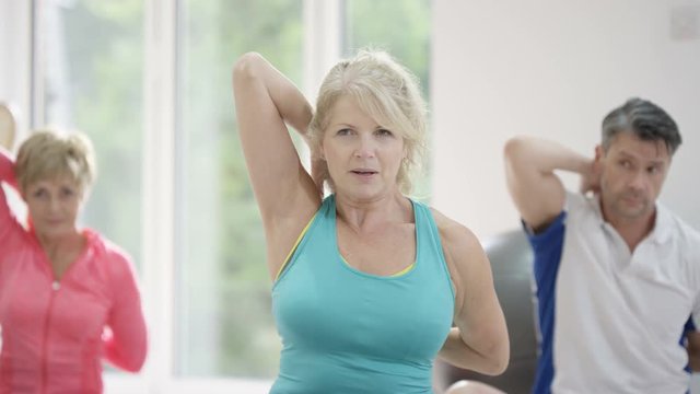  Mature female fitness instructor working out with 2 clients in exercise class