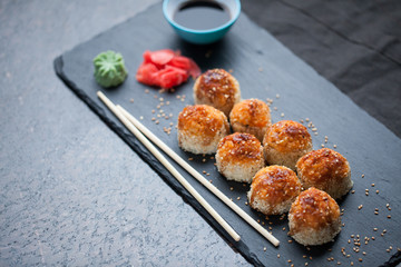 Japanese cuisine. Baked (hot) sushi with crab meat and cheese on a stone slab on a black granite background. Top view with copy space