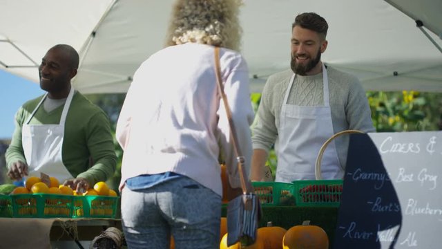  Cheerful man selling fresh fruit & veg to customers at outdoor farmers market