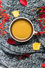 Mug of hot coffee in autumn setting on a wooden table with a knitted scarf, sweater. Comfort, warmth, cozy.
