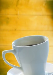 White coffee cup and saucer against blurry yellow wood panel