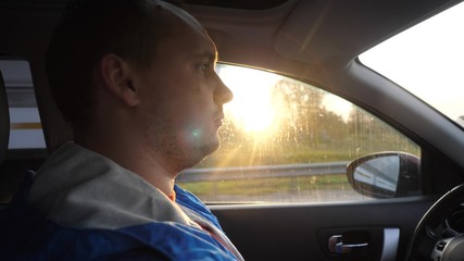 Young man driving the car under sunset sky at outdoor. Summer time.
