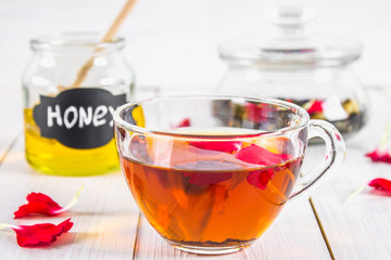 Floral black tea, honey can, petals on a white wooden table.