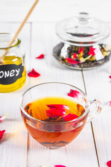 Floral black tea, honey can, petals on a white wooden table.
