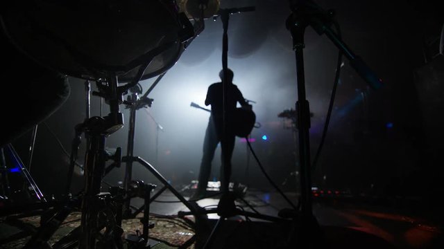  Live band performing on stage at music event, view from behind drum kit.