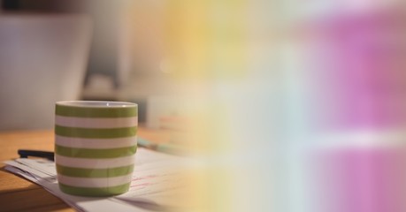 Green and white coffee cup on desk and blurry rainbow transition