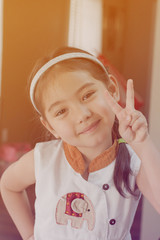 close up smiling little girl with victory finger sign, filtered tones