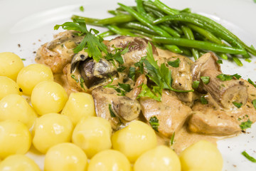 Pork tenderloin with potatoes and wild mushroom sauce and green beans on white plate. Close up.