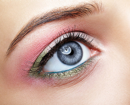 Closeup macro image of human woman eye with pink and green makeup