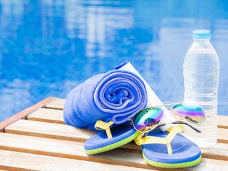 Fototapeta na wymiar flip flops, sunglasses and blue towel at the side of swimming pool. Vacation, beach, summer travel concept