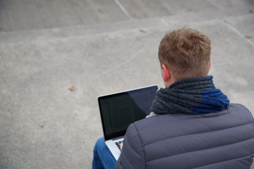 A young man is sitting and working outside with a laptop