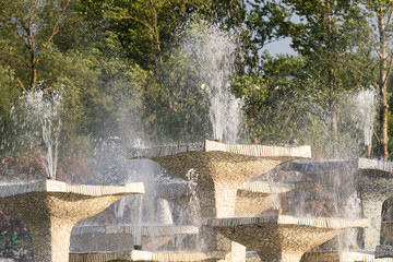 Fototapeta premium Closeup of stone fountain with dripping water and green trees background