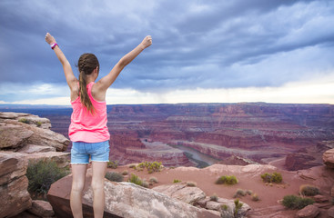 Young woman viewing the beautiful scenic overlook of Dead Horse Point. She is raising her hands in amazement