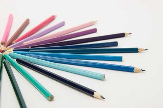 A group of pencils folded in rainbow colors in a circle on a white background
