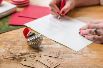 young woman writing christmas cards with red nails, a red pen, and holiday decorations