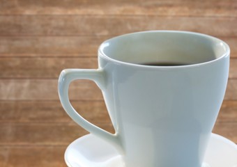 White coffee cup with saucer against blurry wood panel