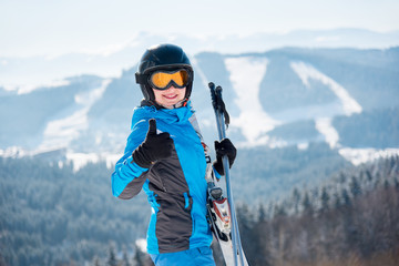 Fototapeta na wymiar Close-up portrait of female skier in a ski mask smiling showing thumbs up at winter ski resort in the mountains copyspace