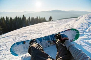 Fotobehang Wintersport Point of view shot of a female snowboarder lying on the snow on the slope relaxing after riding, enjoying stunning view of winter mountains and sunset POV concept  © anatoliy_gleb