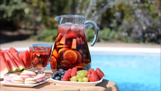 Summer pool party - sangria pitcher with glasses, fresh fruit and French  macaroons on a table near a turquoise swimming pool in a garden setting  Stock Video