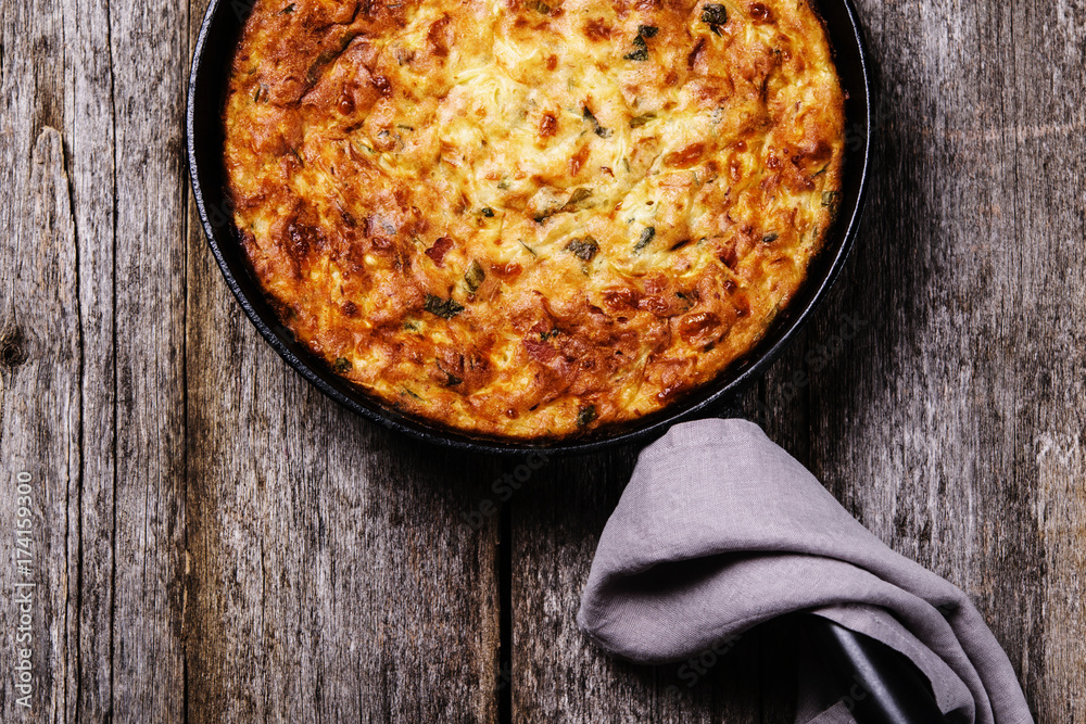 Wall mural Zucchini, bacon and cheese casserole or gratin in cast-iron pan on vintage wooden table. Selective focus 