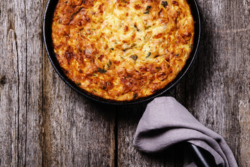 Zucchini, bacon and cheese casserole or gratin in cast-iron pan on vintage wooden table. Selective focus 