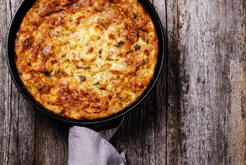 Zucchini, bacon and cheese casserole or gratin in cast-iron pan on vintage wooden table. Selective focus 