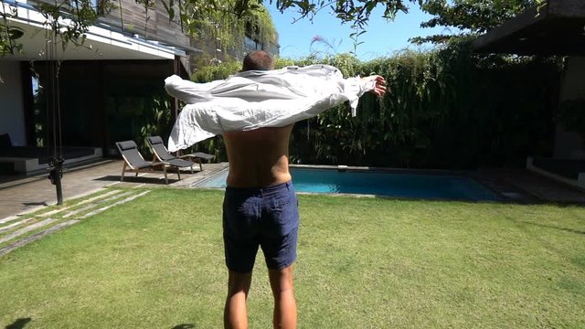 Man standing in his garden and puts shirt on, slow motion shot at 240fps, steadycam shot
