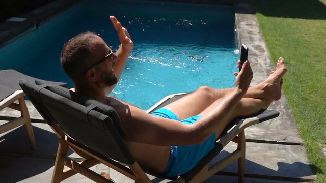 Man lying on the sunbed and having a videocall on smartphone, slow motion shot at 240fps, steadycam shot
