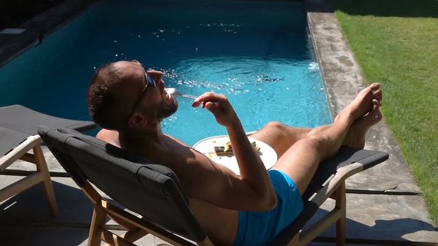 Man lying on sunbed and eating tasty lunch, slow motion shot at 240fps, steadycam shot
