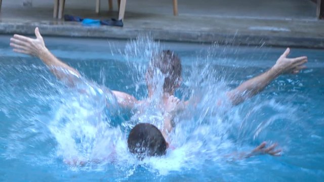 Boy falling into the swimming pool while relaxing with father, slow motion shot at 240fps, steadycam shot
