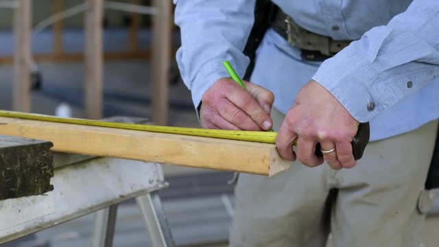 Detail of a contractor measuring and marking up a piece of wood with a pencil, ready to saw inside home under construction. Slow motion 4K recorded at 60fps with slider move.
