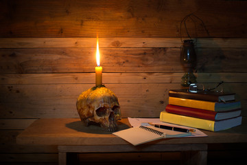 Skull with candle and books for learn and write on the desk in Halloween dark night