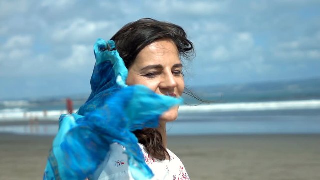 Happy woman holding scarf on the windy beach, slow motion shot at 240fps, steadycam shot
