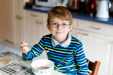 Happy little blond kid boy eating cereals for breakfast or lunch. Healthy eating for children.