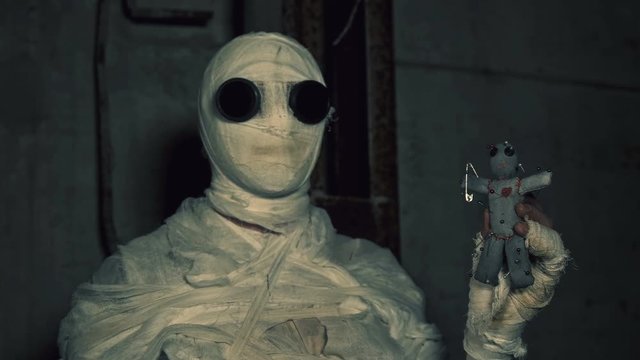 people being in bandages in a dark, abandoned building holding a voodoo doll for ritual