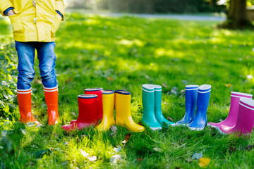 Little kid, boy or girl in jeans and yellow jacket in colorful rain boots.
