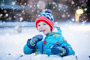 Happy kid boy having fun with snow in winter