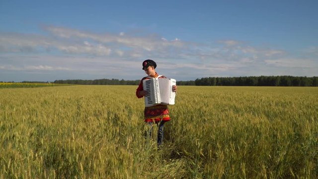 Accordionist in a Russian traditional costume standing in a wheat field and playing the accordion.
