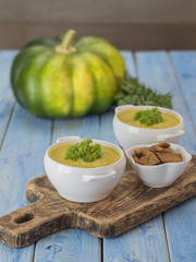 Traditional pumpkin soup with green pumpkin on a wooden board. 