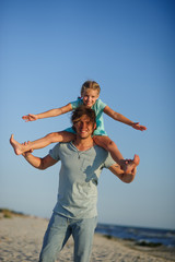 The young man gaily spends time with the little daughter on the sandy beach.