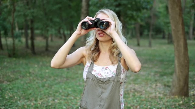 Young woman looking through binoculars and smiling.