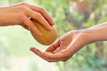 Übergabe von Holzei eine Hand legt das Ei  in die andere Hand