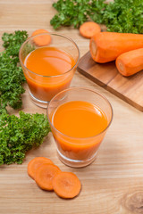 Glass of fresh carrot juice with vegetables on wooden table.