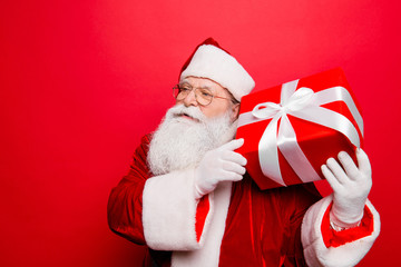 Festive seosonal time of fun and joy. Holly jolly x mas, noel! Grandfather saint nicholas in traditional head wear listening to gift, wondering what`s inside, curious,  isolated on red background