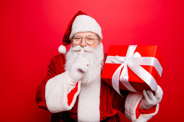 Shh! Keep secret. No sound mute silent confidential, privacy quiet, shush hissing hush concept. Funny Saint Nicholas with forefinger by his lips, holding gift. Festive holly jolly x mas noel