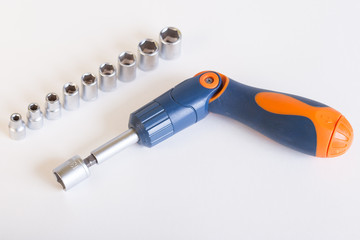 Top view of the screwdriver head. A set of heads and a screwdriver on a light background. Screwdriver with blue - orange handle and a set of heads under the nut.