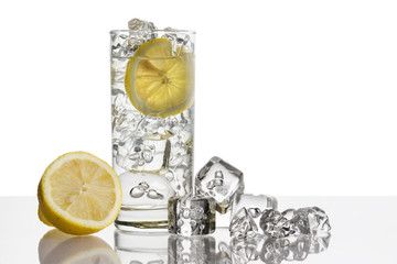 glass full of fresh water with lemon and ice cubes on background