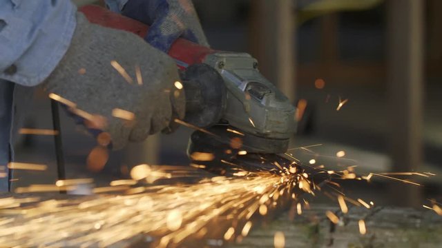 Detail of workman using angle grinder on a piece of metal, creating a shower of sparks inside a house under construction. Front view slow motion 4K recorded at 60fps with slider move.