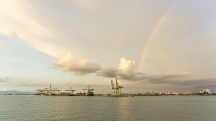 Naklejka na ściany i meble view of far away shipping port with rainbow and beautiful cloud at sunset